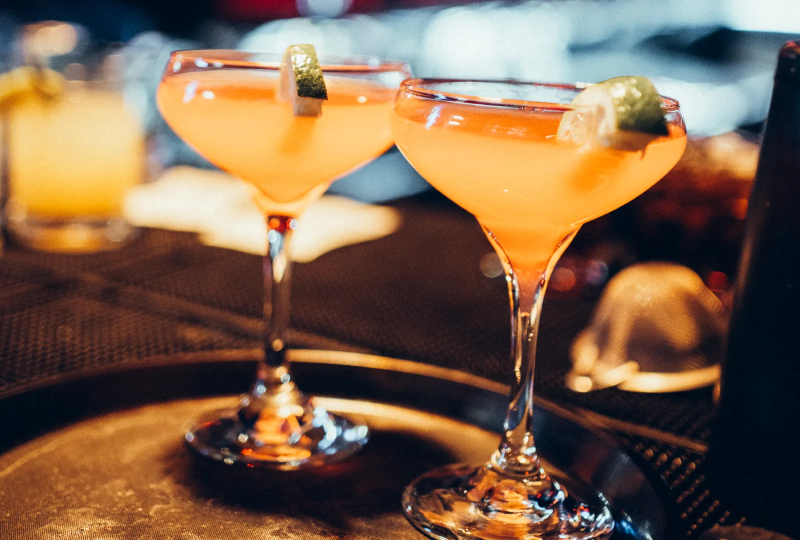 Two orange cocktails garnished with lime on a table
